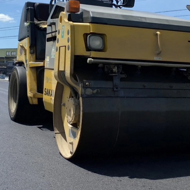 オレンジ色のロードローラーが道路を舗装している画像